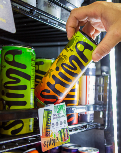A hand placing a SHIMA seltzer can on a store shelf